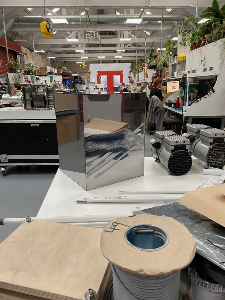 A miniature prototype of a mirrored cube on a table in a model-making workshop.